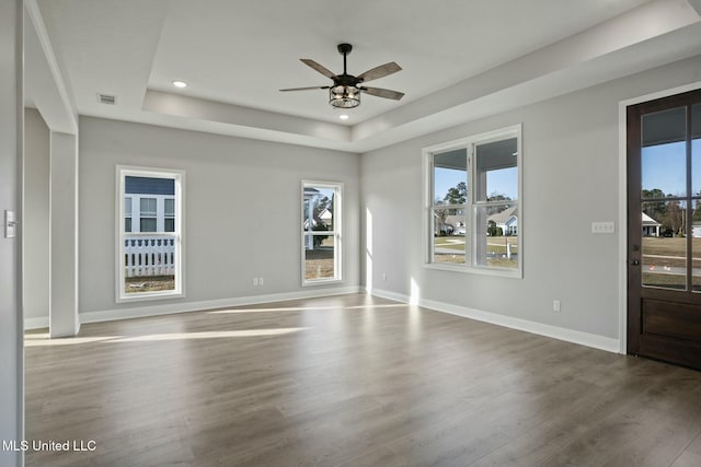 empty room with a tray ceiling, wood finished floors, and baseboards