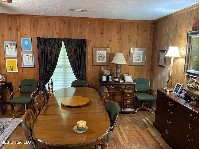 dining room featuring ornamental molding, a textured ceiling, hardwood / wood-style flooring, and wooden walls