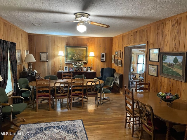 dining room with hardwood / wood-style floors, ceiling fan, a textured ceiling, ornamental molding, and wooden walls