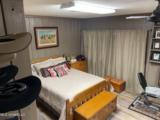 bedroom with light hardwood / wood-style flooring, a textured ceiling, and wood walls