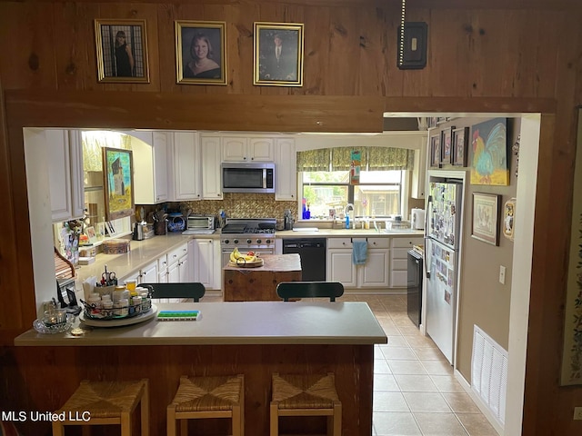 kitchen with tasteful backsplash, a kitchen bar, stainless steel appliances, white cabinets, and light tile patterned floors