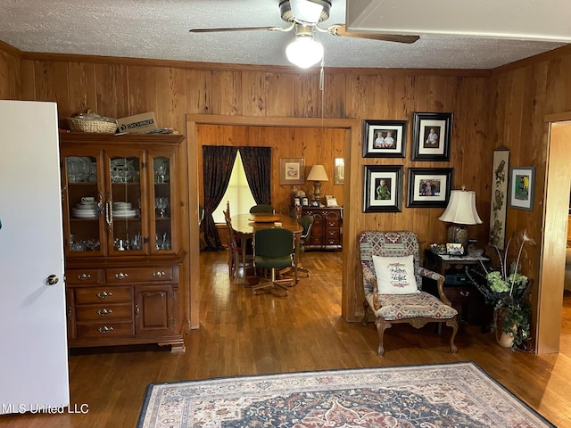 sitting room with wooden walls, dark hardwood / wood-style floors, and ceiling fan