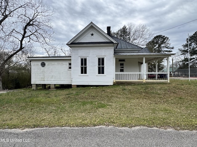 view of front of home featuring a front yard, covered porch, metal roof, and a chimney