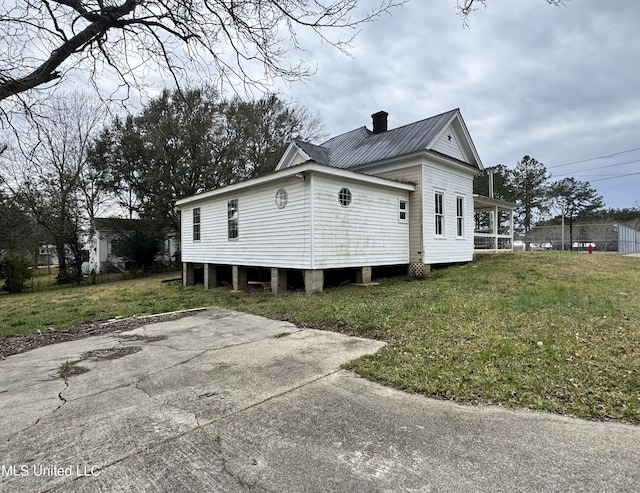 view of side of home featuring a chimney, metal roof, and a yard