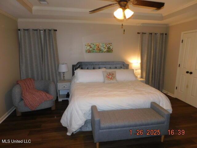 bedroom with dark hardwood / wood-style flooring, a tray ceiling, crown molding, and ceiling fan