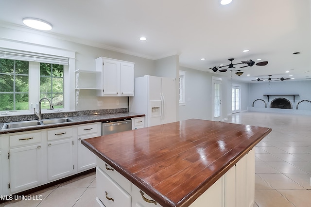 kitchen featuring white cabinetry, white refrigerator with ice dispenser, sink, and a brick fireplace