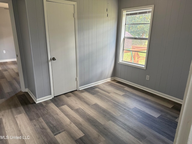 unfurnished bedroom with multiple windows, wooden walls, and wood-type flooring