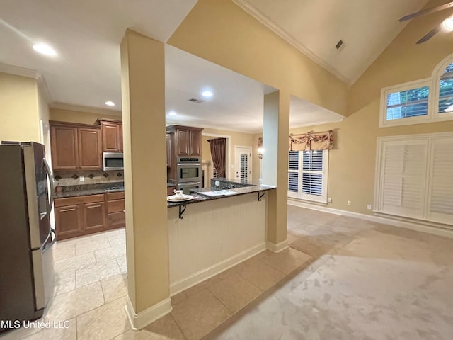 kitchen featuring a kitchen bar, stainless steel appliances, lofted ceiling, ornamental molding, and light colored carpet