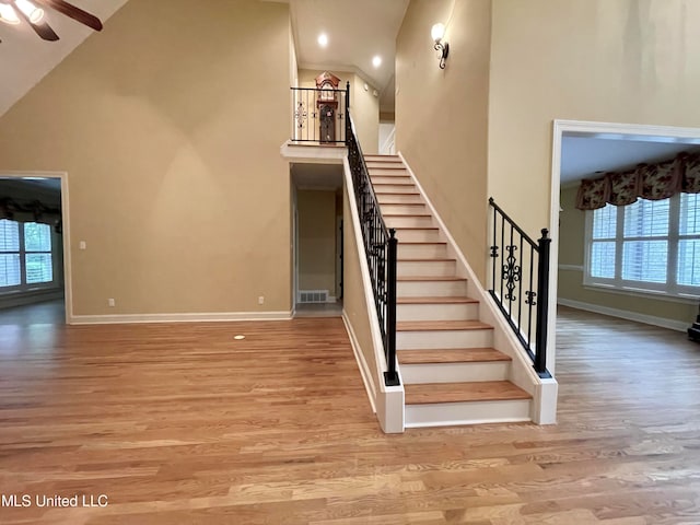 staircase featuring high vaulted ceiling, wood-type flooring, and ceiling fan