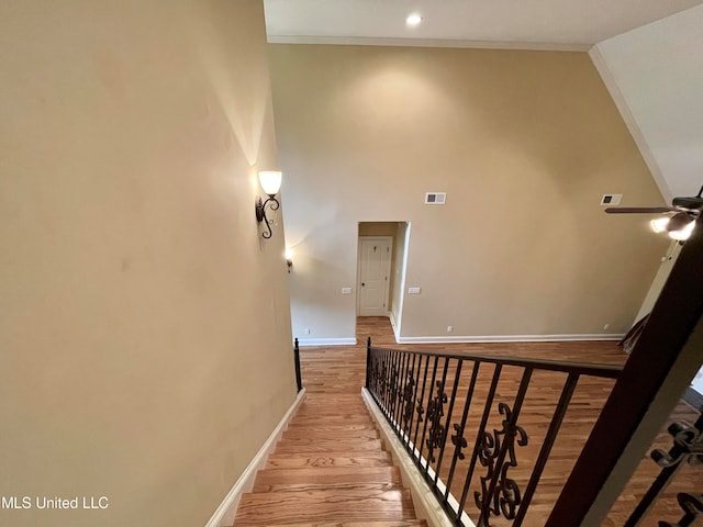 stairs with a towering ceiling, crown molding, and wood-type flooring