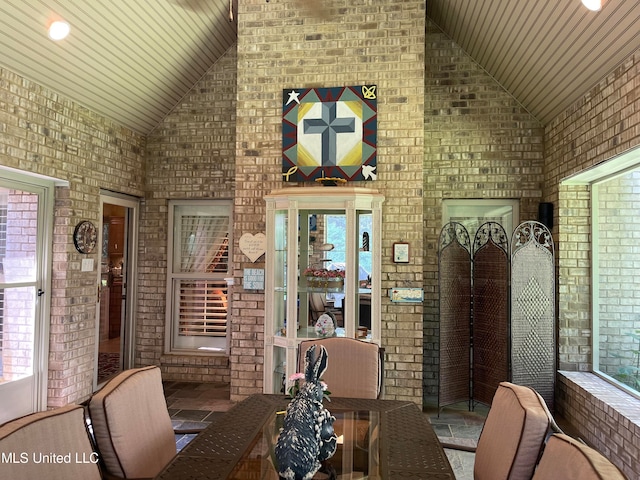 dining room with brick wall, wood ceiling, and high vaulted ceiling