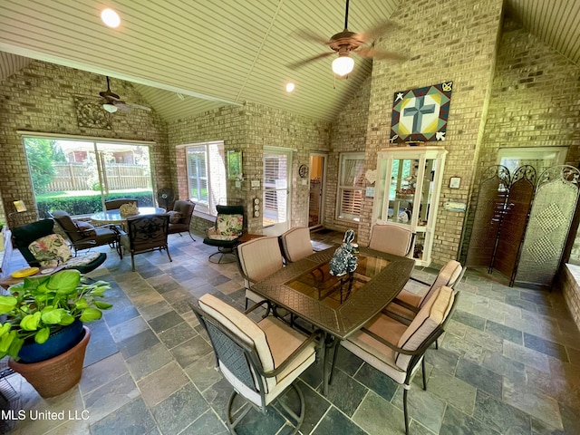 dining room featuring brick wall, high vaulted ceiling, and ceiling fan