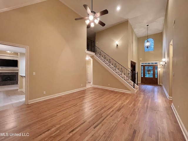 unfurnished living room featuring ornamental molding, hardwood / wood-style floors, ceiling fan with notable chandelier, and high vaulted ceiling