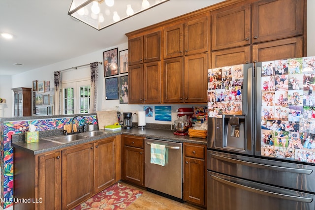 kitchen with stainless steel appliances, a sink, a peninsula, dark countertops, and brown cabinetry