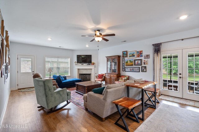 living room with french doors, wood finished floors, a tiled fireplace, a ceiling fan, and recessed lighting