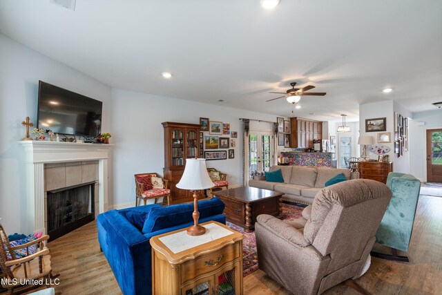 living area with wood finished floors, a tile fireplace, a ceiling fan, and recessed lighting