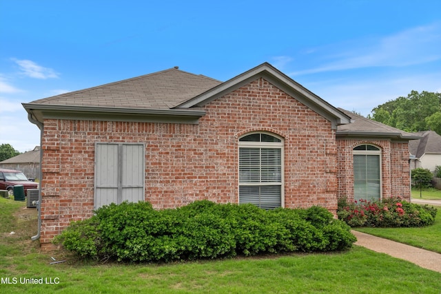 view of side of property featuring brick siding, a shingled roof, and a yard
