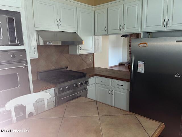 kitchen with tile counters, extractor fan, white cabinetry, appliances with stainless steel finishes, and tasteful backsplash