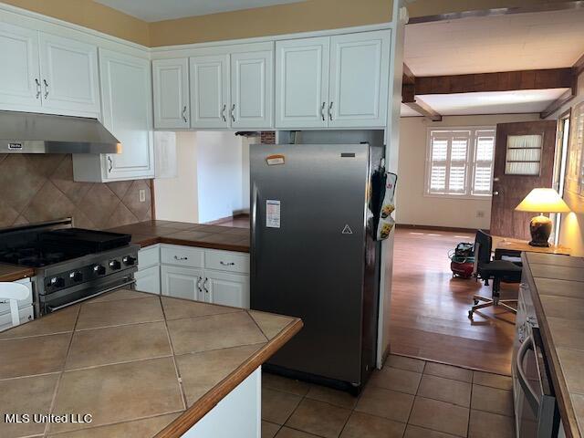 kitchen with tile counters, white cabinets, black electric range oven, and stainless steel refrigerator