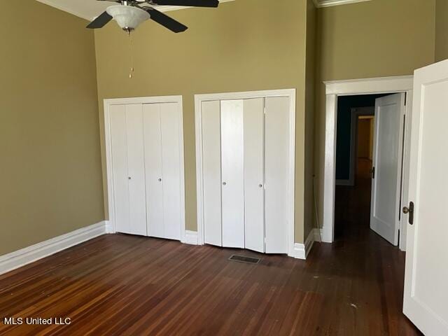 unfurnished bedroom featuring multiple closets, a high ceiling, dark hardwood / wood-style floors, and ceiling fan