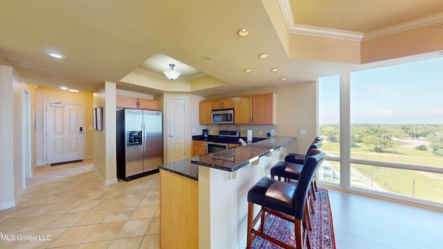 kitchen featuring kitchen peninsula, a breakfast bar area, dark stone countertops, crown molding, and stainless steel appliances