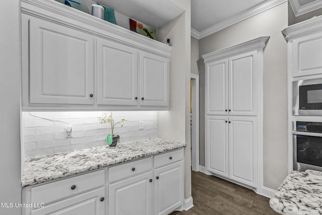 kitchen with dark wood finished floors, crown molding, backsplash, appliances with stainless steel finishes, and white cabinetry