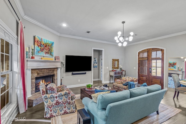 living area with a brick fireplace, a notable chandelier, crown molding, and wood finished floors