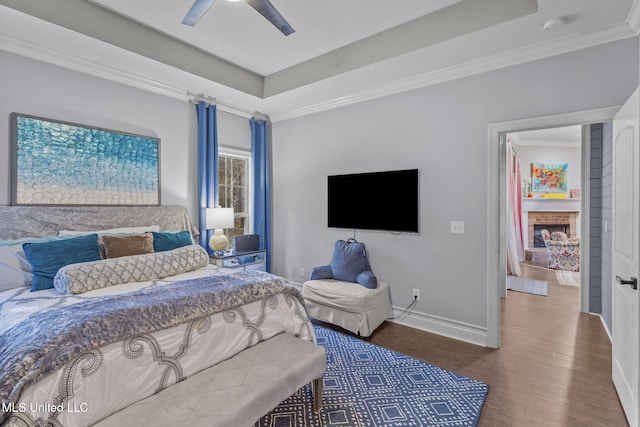 bedroom with ornamental molding, a tray ceiling, baseboards, and wood finished floors