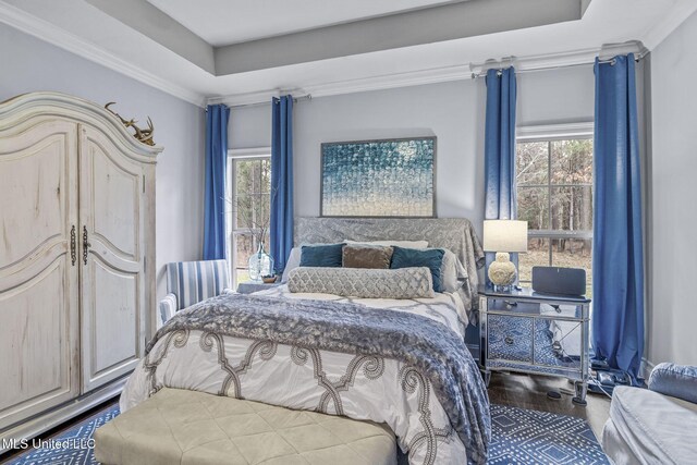 bedroom with ornamental molding, a raised ceiling, multiple windows, and wood finished floors