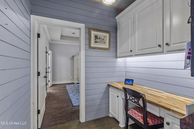 home office featuring crown molding, built in desk, dark wood finished floors, and wooden walls