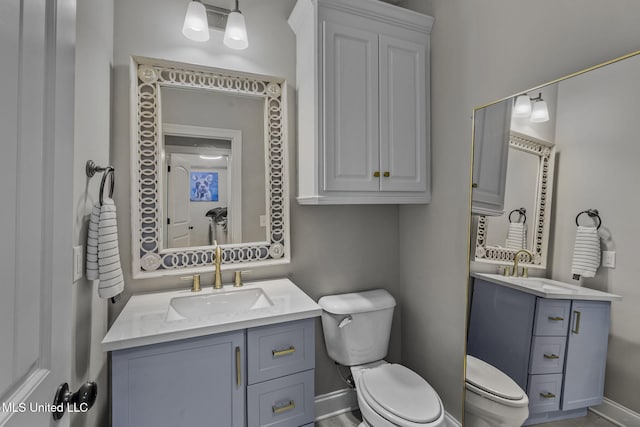 bathroom with two vanities, a sink, toilet, and baseboards