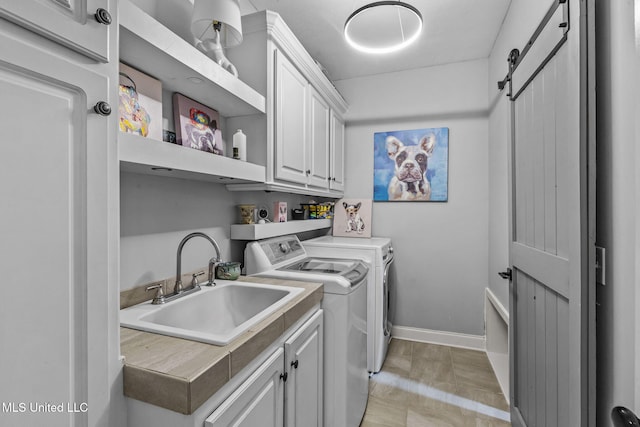 laundry area with cabinet space, a barn door, baseboards, washer and dryer, and a sink