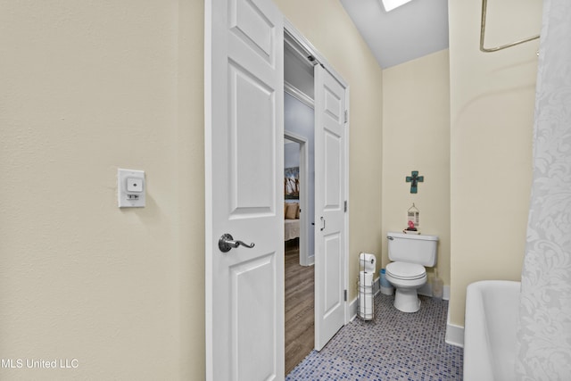 full bathroom with a tub to relax in, a skylight, baseboards, and toilet