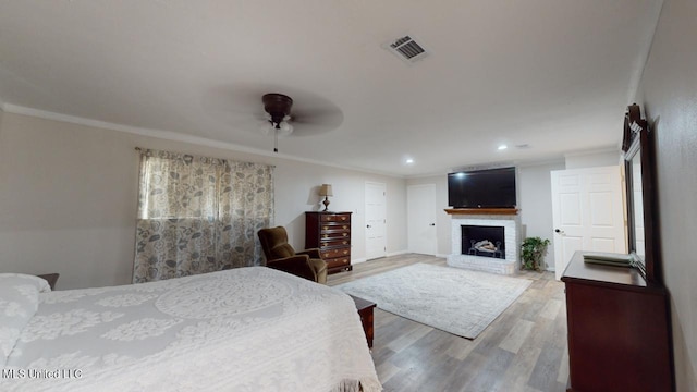 bedroom featuring hardwood / wood-style floors, crown molding, a fireplace, and ceiling fan