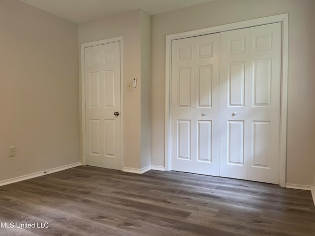 unfurnished bedroom with a closet, a textured ceiling, and dark hardwood / wood-style floors