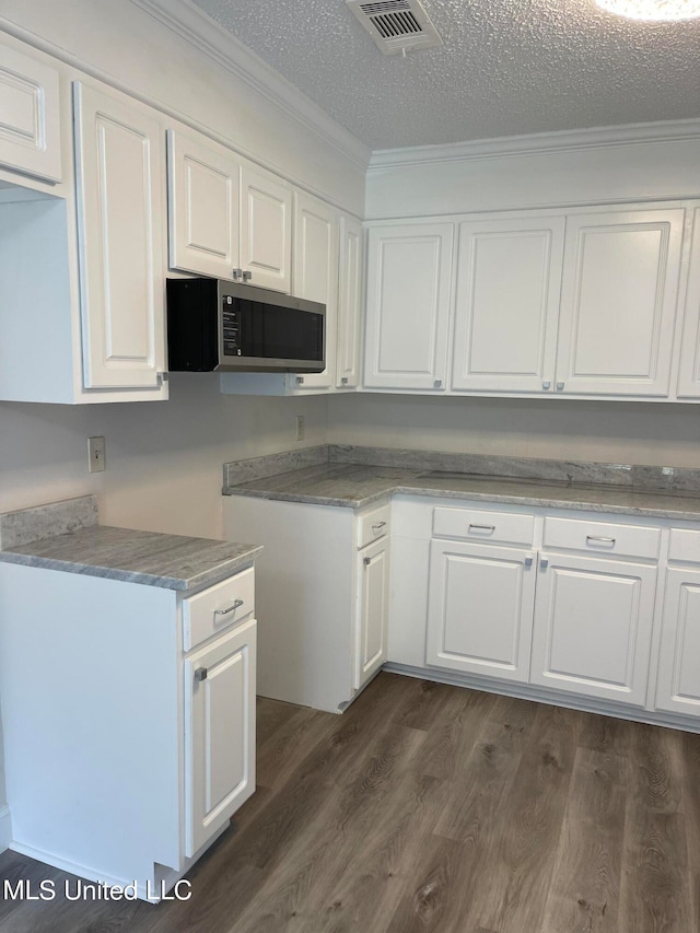 kitchen featuring dark wood-type flooring, a textured ceiling, ornamental molding, and white cabinets