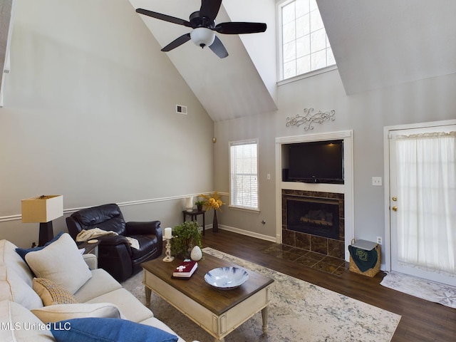 living area with ceiling fan, high vaulted ceiling, a tile fireplace, wood finished floors, and visible vents