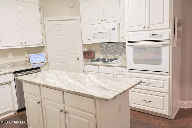 kitchen with white appliances, a center island, light stone countertops, and white cabinets