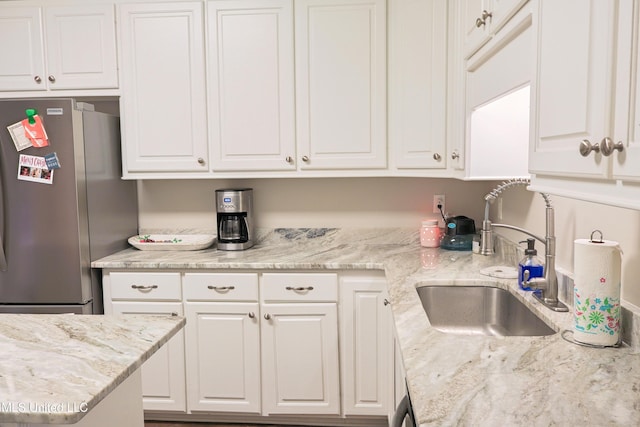 kitchen with white cabinetry, sink, light stone countertops, and stainless steel refrigerator