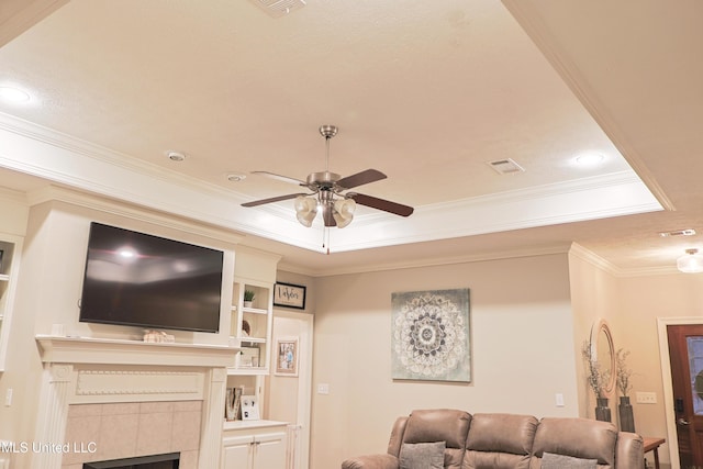 living room with a raised ceiling, crown molding, a fireplace, and ceiling fan