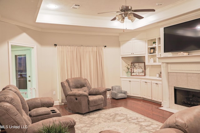 living room featuring a tile fireplace, dark hardwood / wood-style floors, ornamental molding, ceiling fan, and a raised ceiling