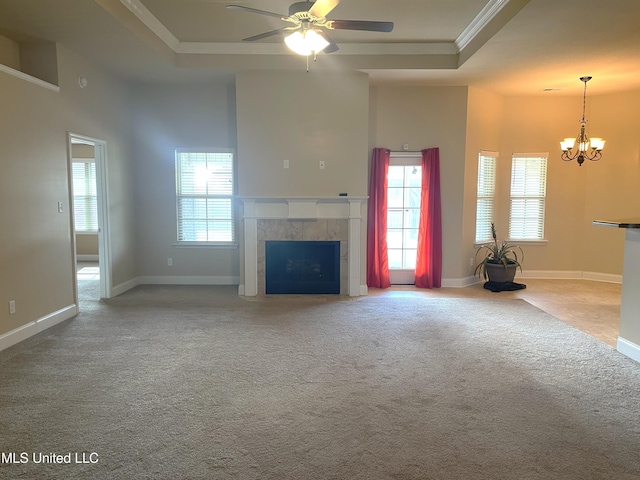 unfurnished living room featuring a tray ceiling, carpet floors, ornamental molding, a tiled fireplace, and ceiling fan with notable chandelier