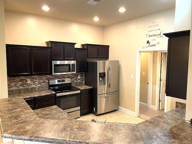 kitchen with tasteful backsplash, kitchen peninsula, dark stone countertops, and appliances with stainless steel finishes