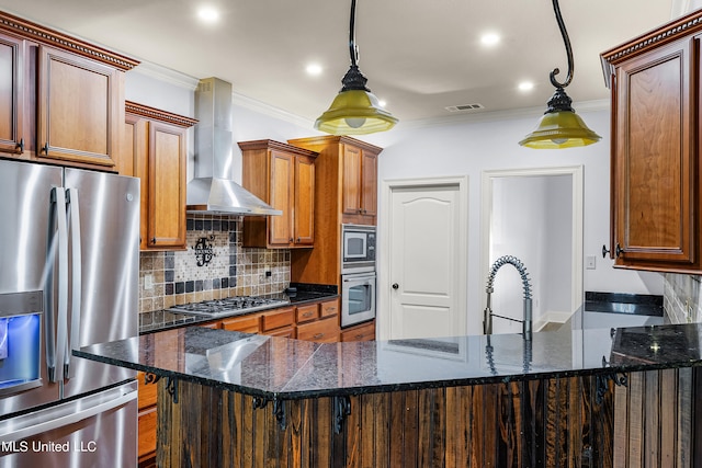 kitchen featuring wall chimney range hood, hanging light fixtures, stainless steel appliances, dark stone countertops, and a breakfast bar area