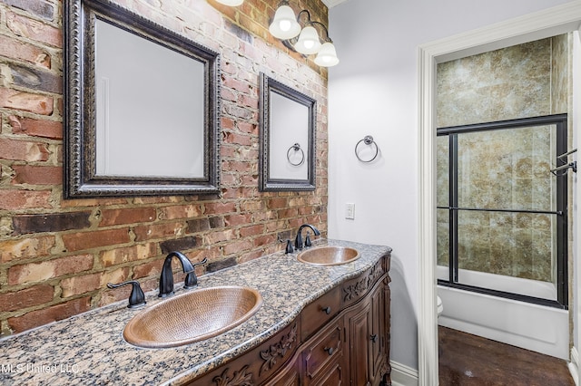 bathroom featuring vanity, combined bath / shower with glass door, and brick wall