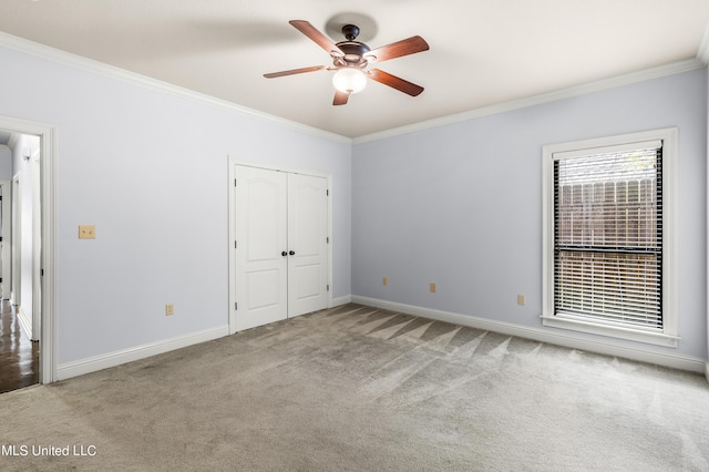 unfurnished bedroom featuring carpet, a ceiling fan, a closet, crown molding, and baseboards