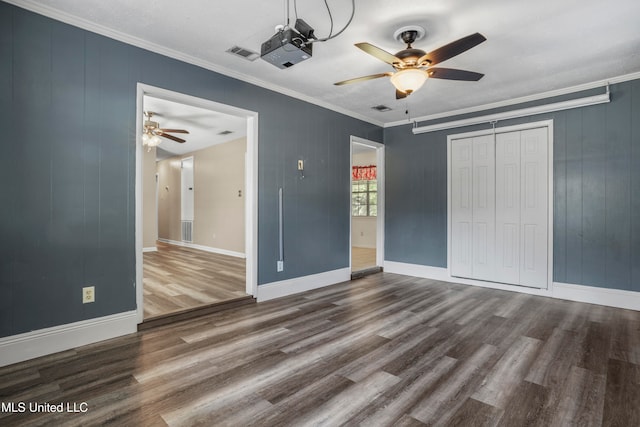 unfurnished bedroom with crown molding, dark hardwood / wood-style flooring, wooden walls, a closet, and ceiling fan