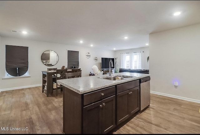 kitchen featuring a center island with sink, light wood-type flooring, dark brown cabinets, stainless steel dishwasher, and sink