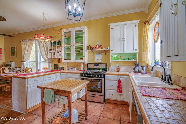 kitchen featuring sink, stainless steel gas stove, white cabinetry, and hanging light fixtures