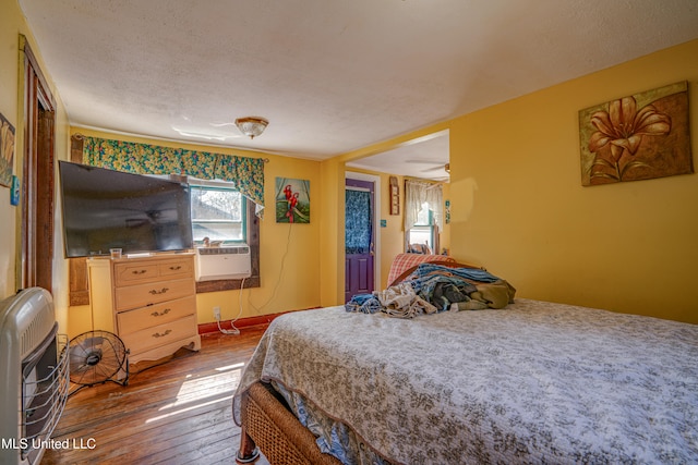 bedroom featuring a textured ceiling, cooling unit, wood-type flooring, and heating unit